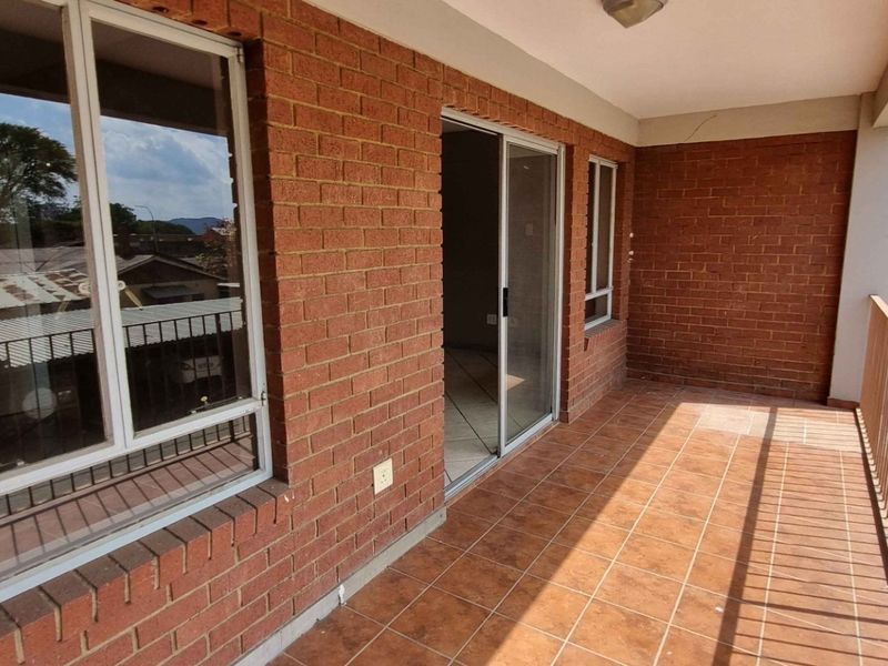 A spacious balcony featuring exposed brick walls, tiled flooring, and a metal balustrade, offering an outdoor extension to the living area.