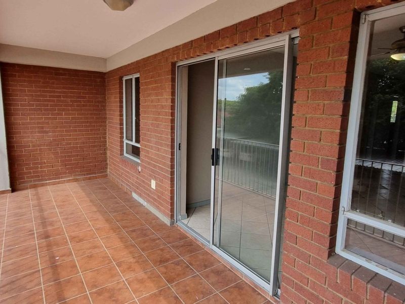 A spacious covered balcony featuring exposed brick walls, tiled flooring, and a sliding glass door providing access to the interior living area.