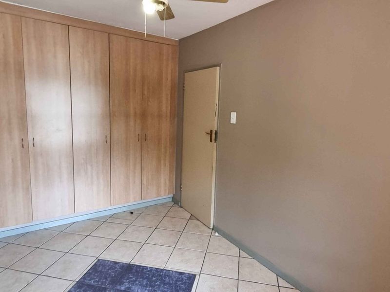 A clean, empty bedroom featuring neutral wall tones, tiled flooring, and ample built-in cupboard storage space.