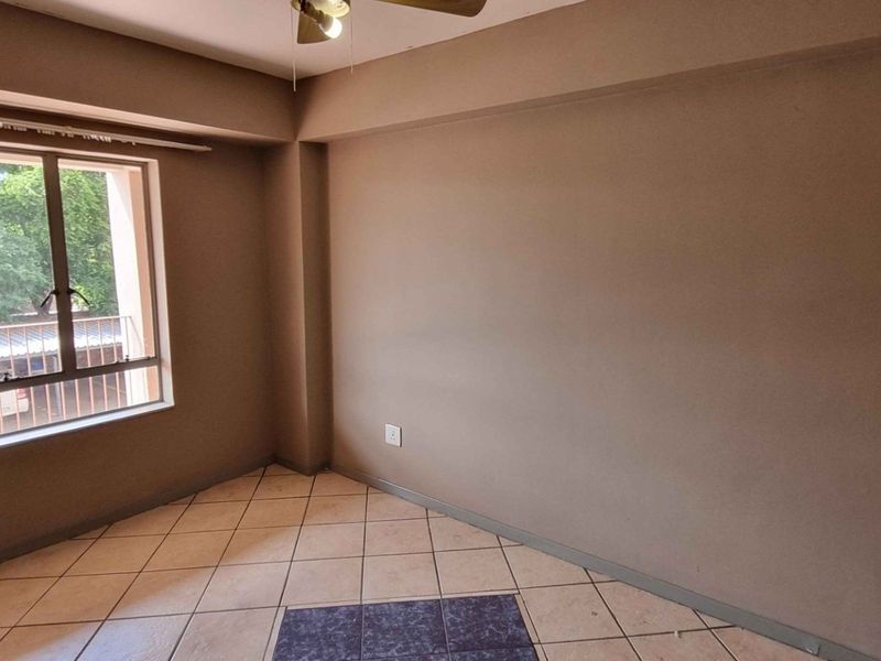 An empty bedroom featuring neutral wall paint, tiled flooring, and a ceiling fan, providing a blank canvas for personalization.
