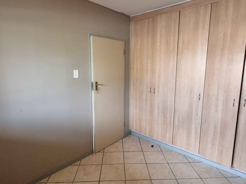 A clean, empty bedroom featuring neutral wall tones, tiled flooring, and extensive built-in wooden cupboards for storage.