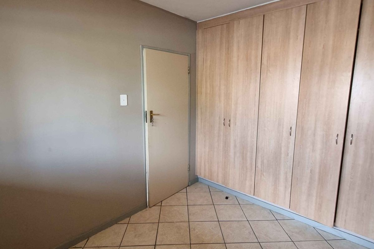 A clean, empty bedroom featuring neutral wall tones, tiled flooring, and extensive built-in wooden cupboards for storage.