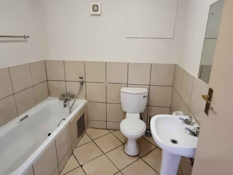 A functional bathroom featuring a bathtub, pedestal basin, and toilet with neutral wall and floor tiling.
