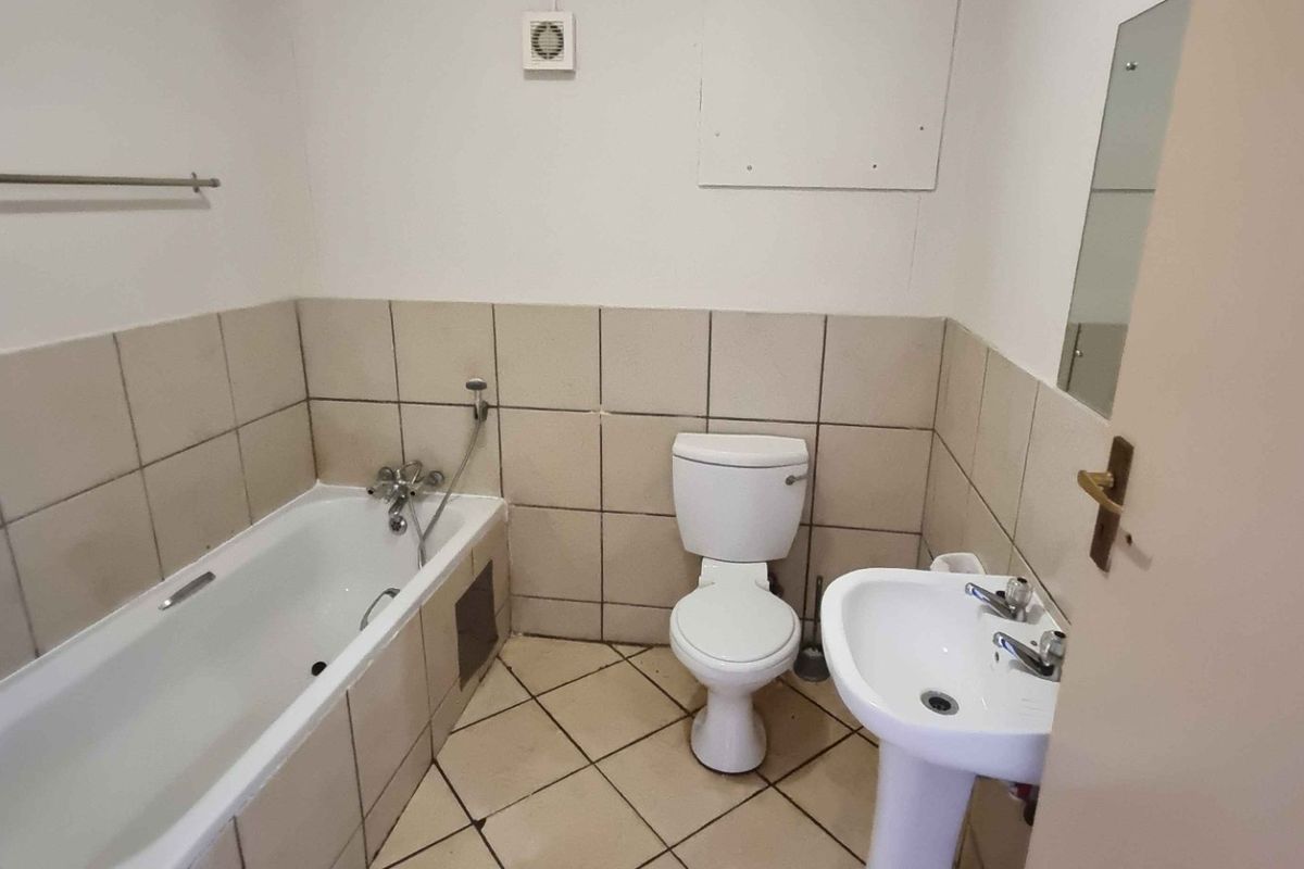 A functional bathroom featuring a bathtub, pedestal basin, and toilet with neutral wall and floor tiling.