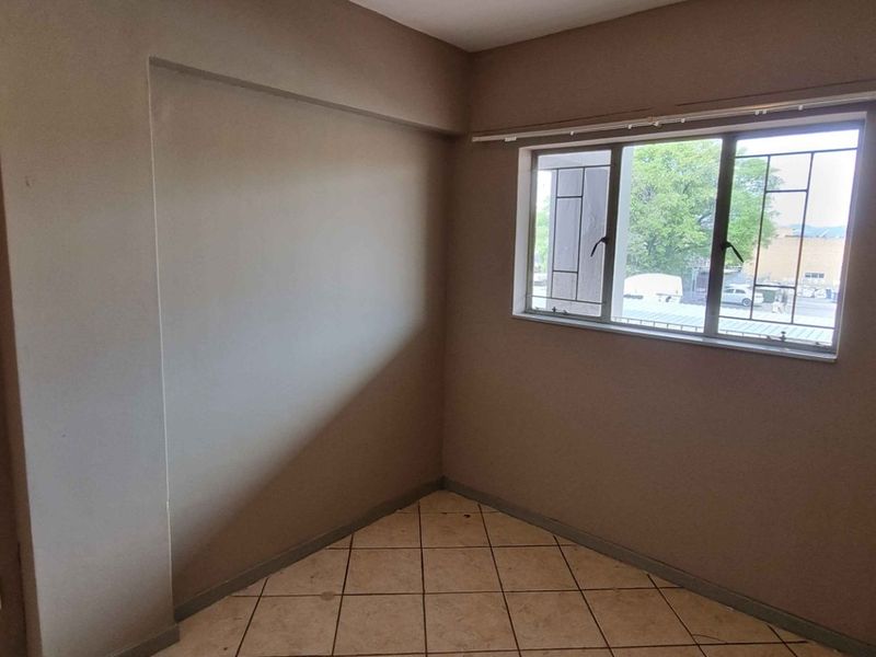 An empty bedroom featuring neutral wall tones, tiled flooring, and an aluminium window with integrated security bars.