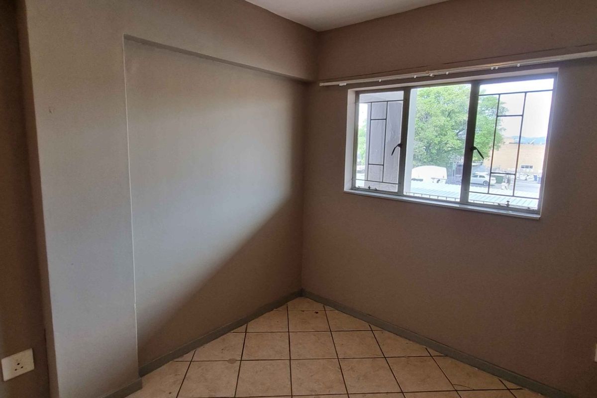 An empty bedroom featuring neutral wall tones, tiled flooring, and an aluminium window with integrated security bars.