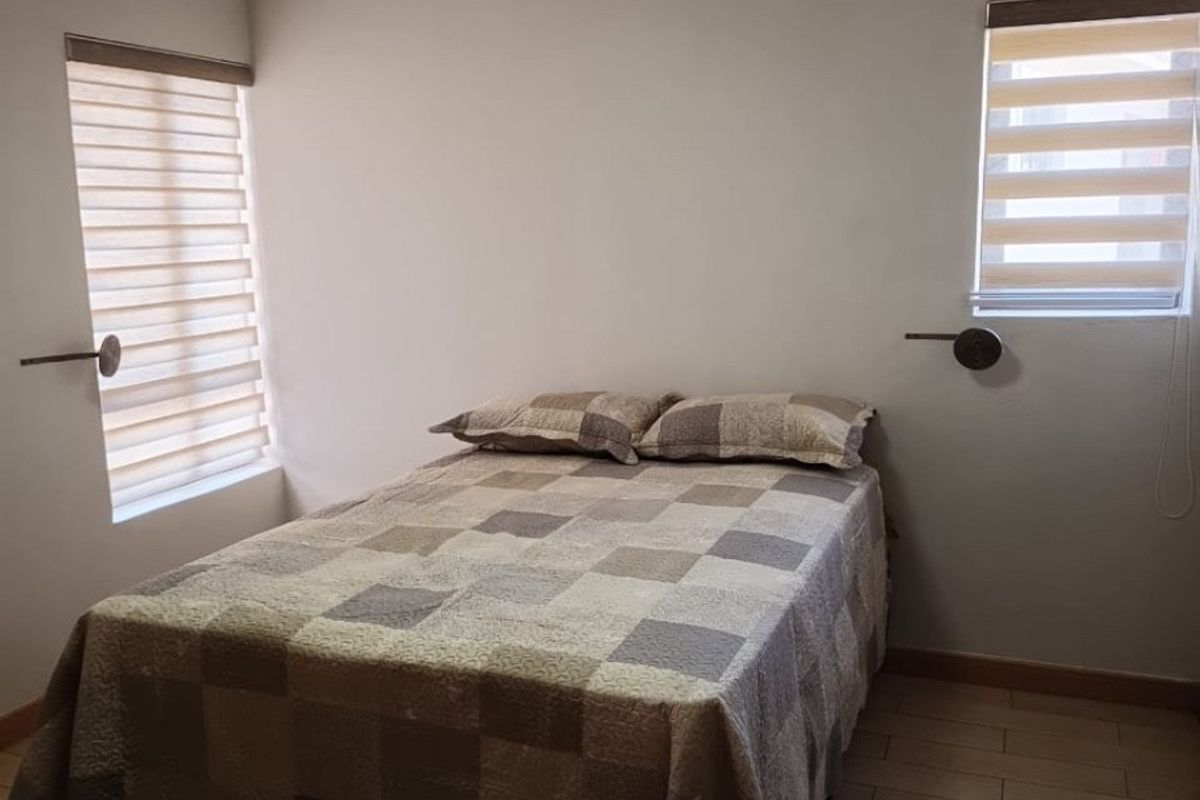 A well-maintained bedroom featuring tiled flooring, dual windows with modern zebra blinds, and wall-mounted lighting fixtures.