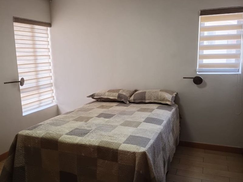 A well-maintained bedroom featuring tiled flooring, dual windows with modern zebra blinds, and wall-mounted lighting fixtures.
