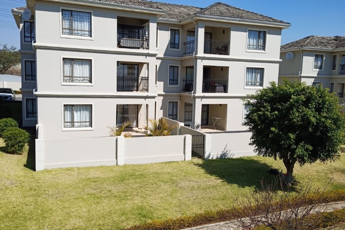 A view of the rear elevation of a multi-story apartment building featuring private balconies, a well-maintained garden, and paved walkways.
