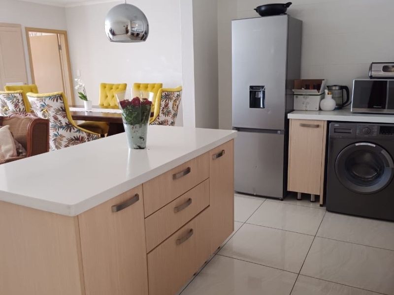 Modern open-plan kitchen featuring a central island with quartz countertops, light wood cabinetry, and tiled flooring, seamlessly flowing into the adjacent dining area.