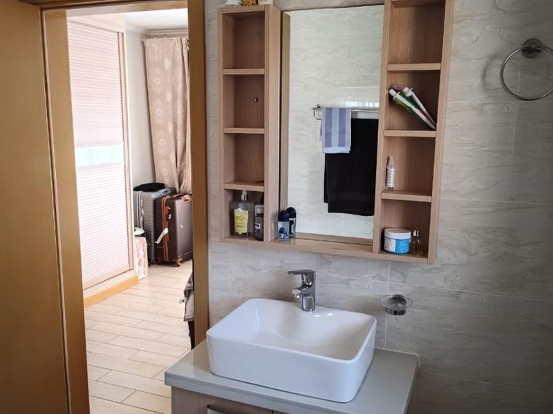 A modern bathroom vanity featuring a white vessel sink, wood-tone cabinetry, and integrated wall shelving against neutral tiled walls.