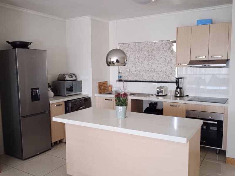 Modern kitchen featuring light wood cabinetry, stone countertops, a central island, and integrated stainless steel appliances with neutral tiled flooring.