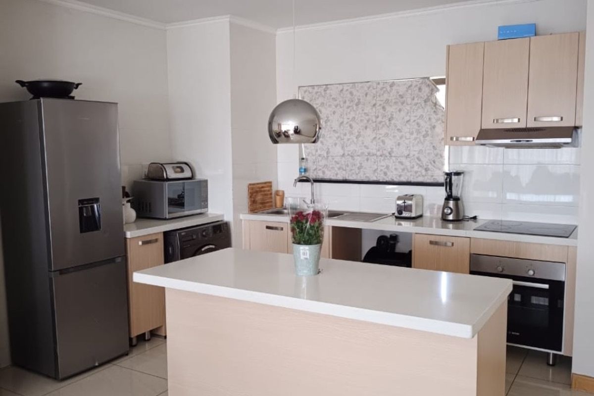 Modern kitchen featuring light wood cabinetry, stone countertops, a central island, and integrated stainless steel appliances with neutral tiled flooring.