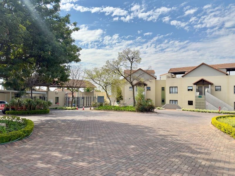 View of the apartment complex entrance featuring a paved driveway, landscaped garden beds, and secure gated access.