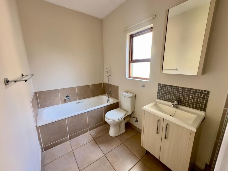 A clean and functional bathroom featuring a bathtub, toilet, and a vanity unit with a basin, finished with neutral floor and wall tiling.