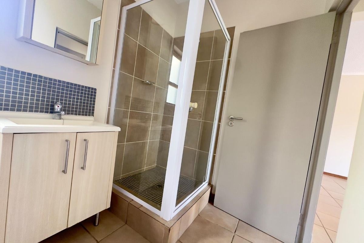 A clean and functional bathroom featuring a glass shower enclosure, a modern vanity cabinet with basin, and neutral wall and floor tiling.