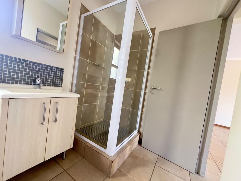 A clean and functional bathroom featuring a glass shower enclosure, a modern vanity cabinet with basin, and neutral wall and floor tiling.