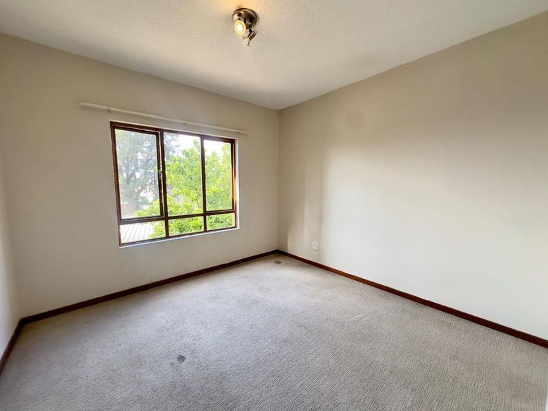An empty bedroom featuring neutral walls, carpet flooring, and a large window with timber frames, offering a blank canvas for personalization.