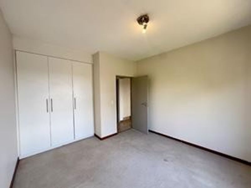A vacant bedroom featuring built-in cupboards, neutral wall finishes, and carpeted flooring, offering a blank canvas for personalization.