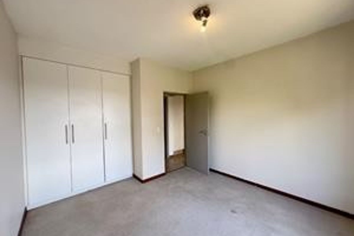 A vacant bedroom featuring built-in cupboards, neutral wall finishes, and carpeted flooring, offering a blank canvas for personalization.
