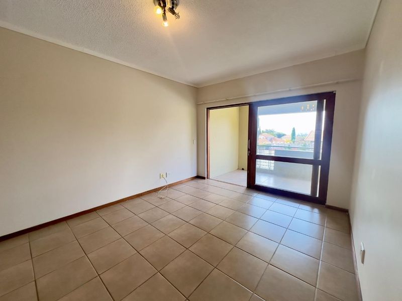 An empty living room featuring neutral tiled flooring and a sliding glass door providing access to an outdoor balcony area.