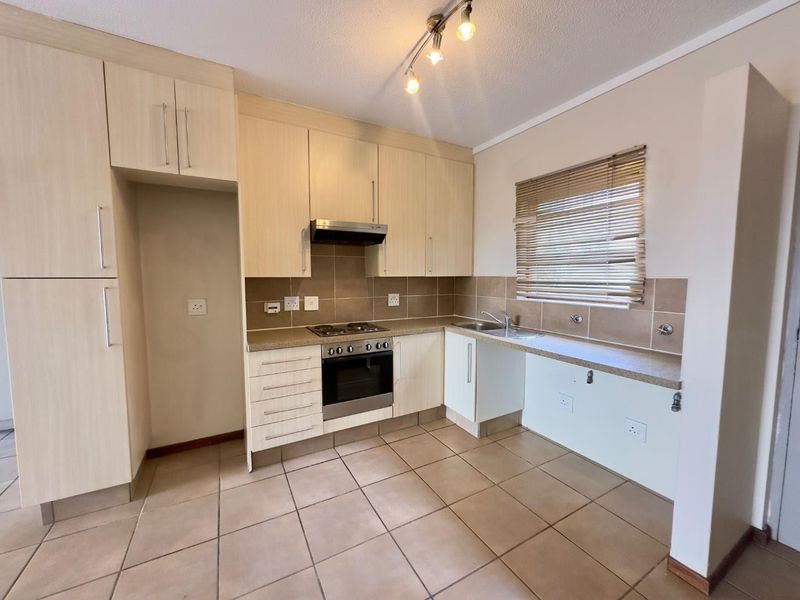 A functional kitchen featuring light wood-finish cabinetry, tiled flooring, a built-in oven and hob, and a tiled backsplash with ample counter space.