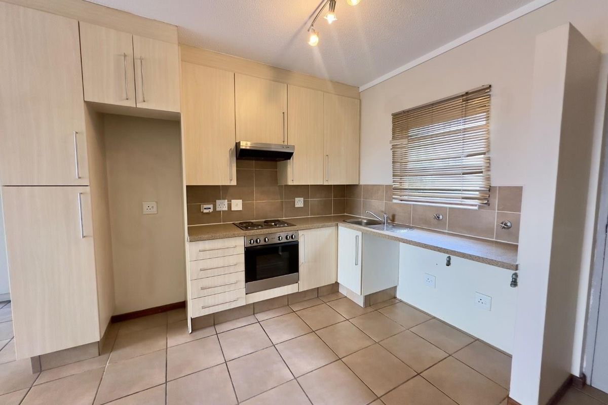 A functional kitchen featuring light wood-finish cabinetry, tiled flooring, a built-in oven and hob, and a tiled backsplash with ample counter space.