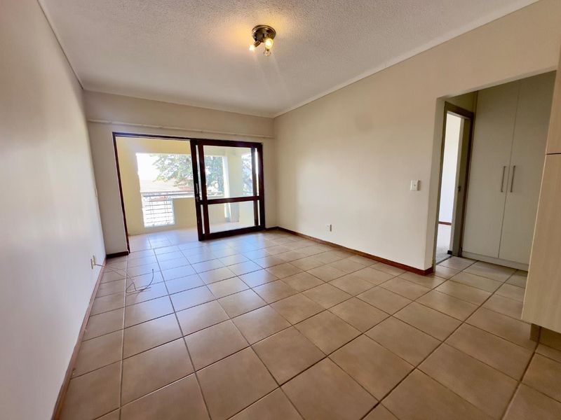 An empty living room featuring ceramic floor tiles, a sliding glass door leading to a balcony, and built-in storage cupboards.