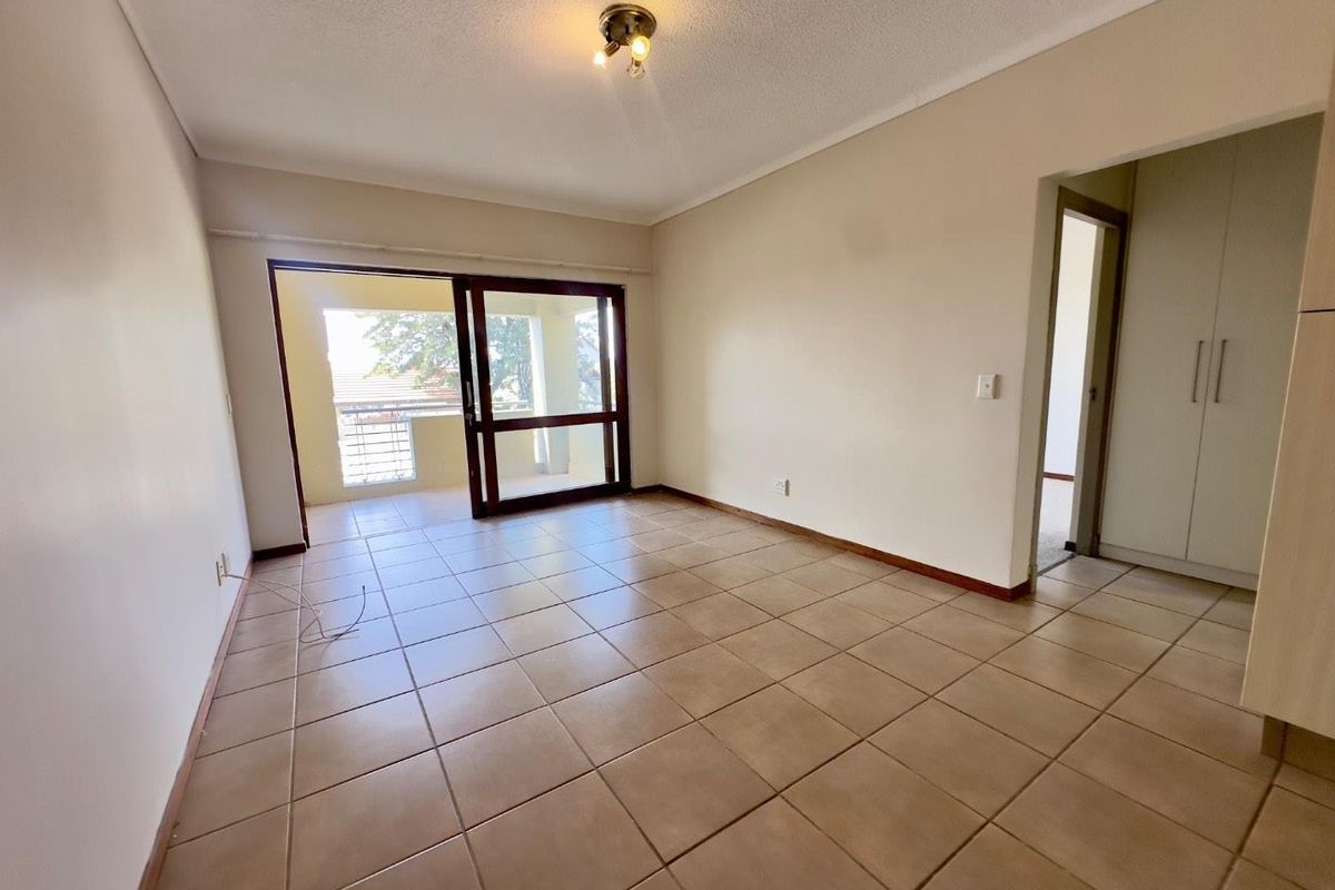 An empty living room featuring ceramic floor tiles, a sliding glass door leading to a balcony, and built-in storage cupboards.