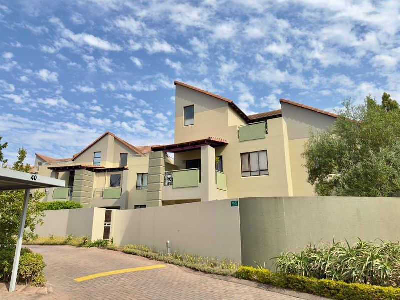 Exterior view of a multi-story apartment complex featuring tiled roofs, private balconies, and a paved driveway with a covered carport.