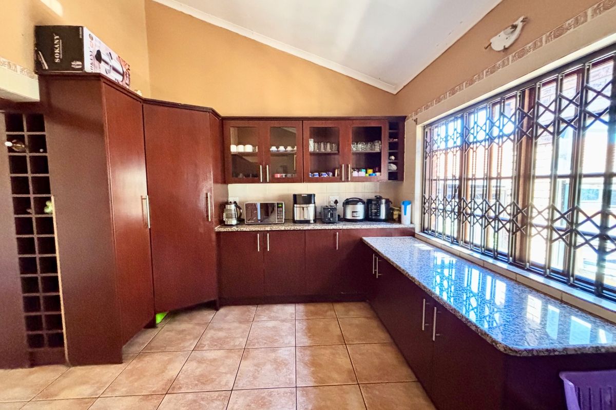 A functional kitchen featuring dark wood cabinetry, granite countertops, tiled flooring, and a large window with security bars, set under a vaulted ceiling.