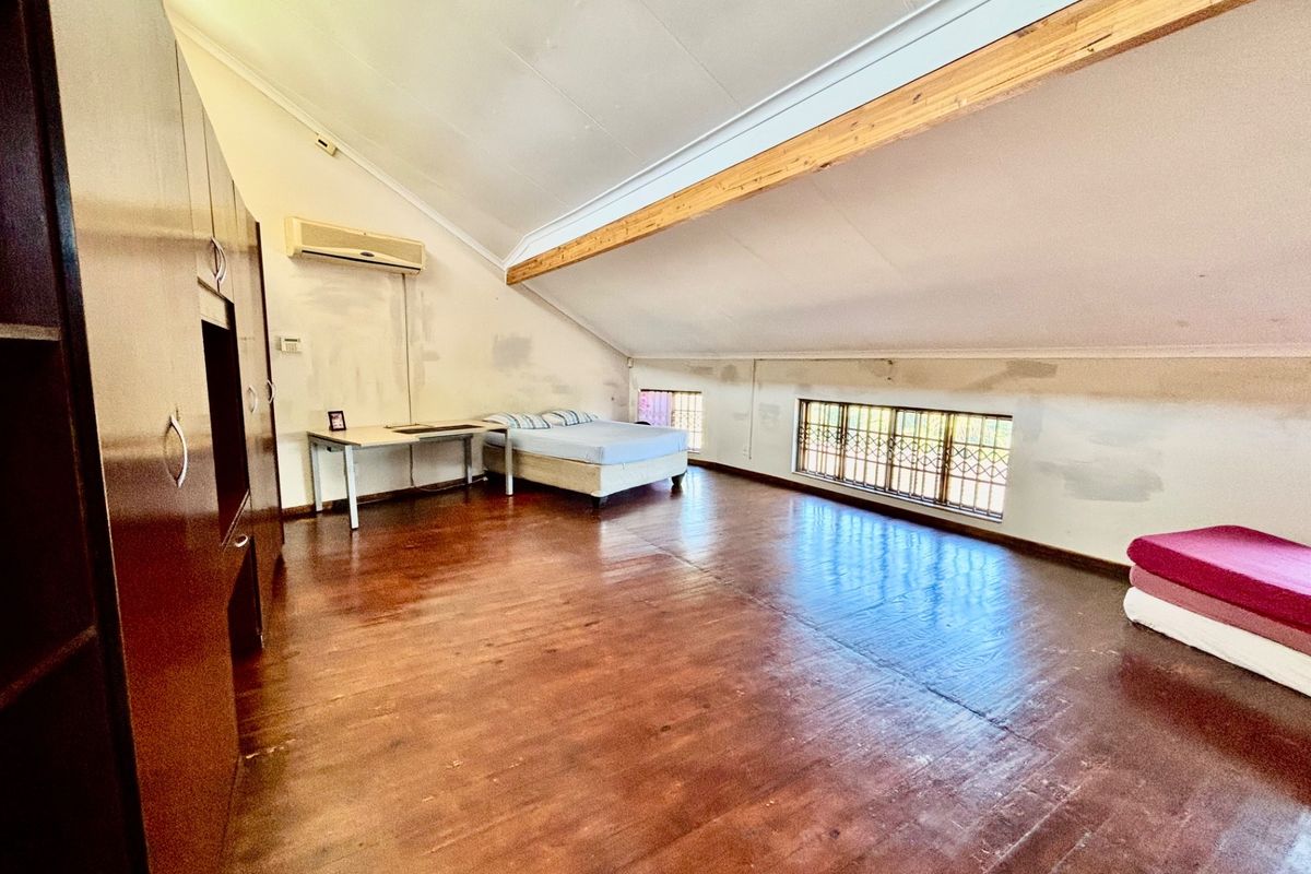 Spacious attic-style bedroom featuring vaulted ceilings with exposed timber beams, built-in cabinetry, air conditioning, and timber flooring, requiring cosmetic wall finishing.