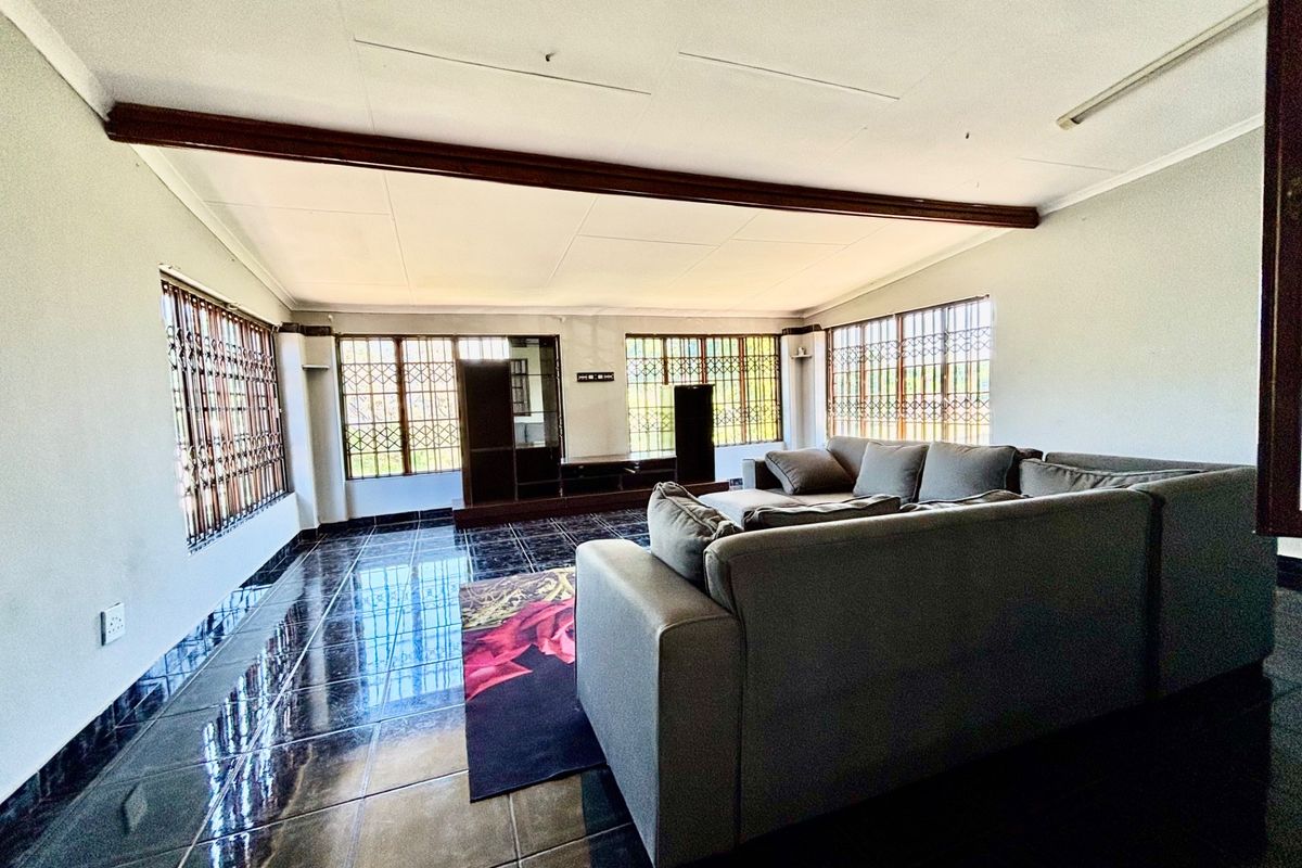 Spacious living room featuring dark tiled flooring, large windows with security bars, and a prominent exposed ceiling beam.