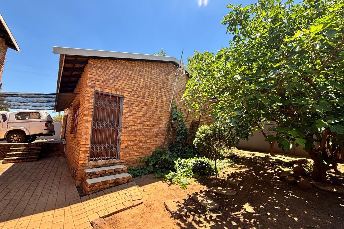 Rear exterior view of a face brick house featuring a paved walkway, security gate entrance, and established garden area.