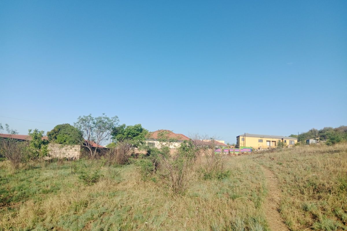 A view of a vacant residential plot featuring natural vegetation and surrounding boundary walls, offering potential for future development.