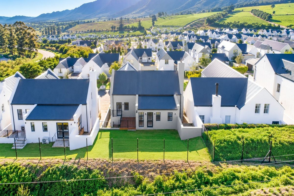 Aerial view of a modern residential property featuring a corrugated metal roof, timber deck, and well-maintained garden within a scenic estate setting.