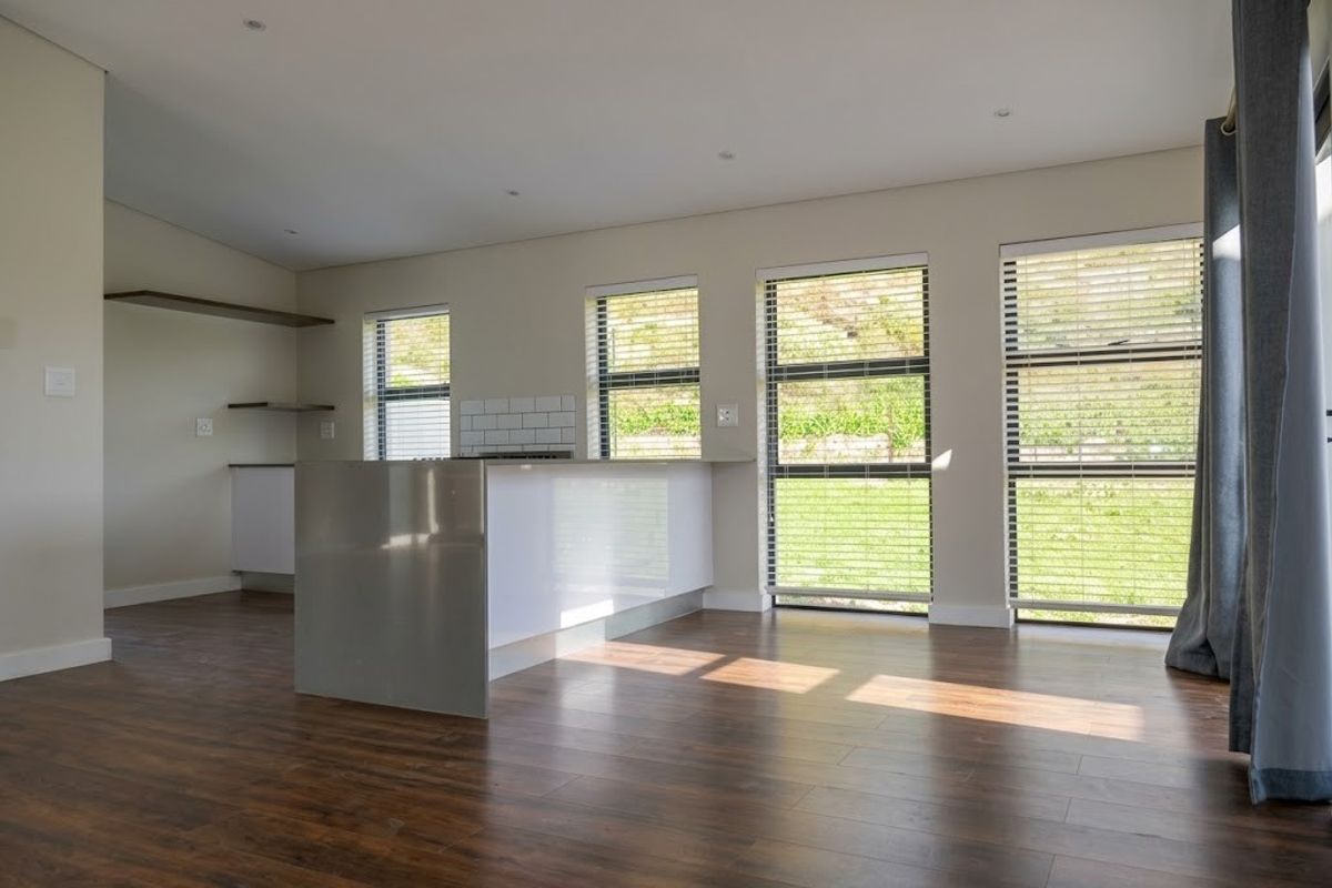 Modern kitchen featuring a sleek island, subway tile backsplash, floating shelving, and large windows with venetian blinds, set against dark laminate flooring.