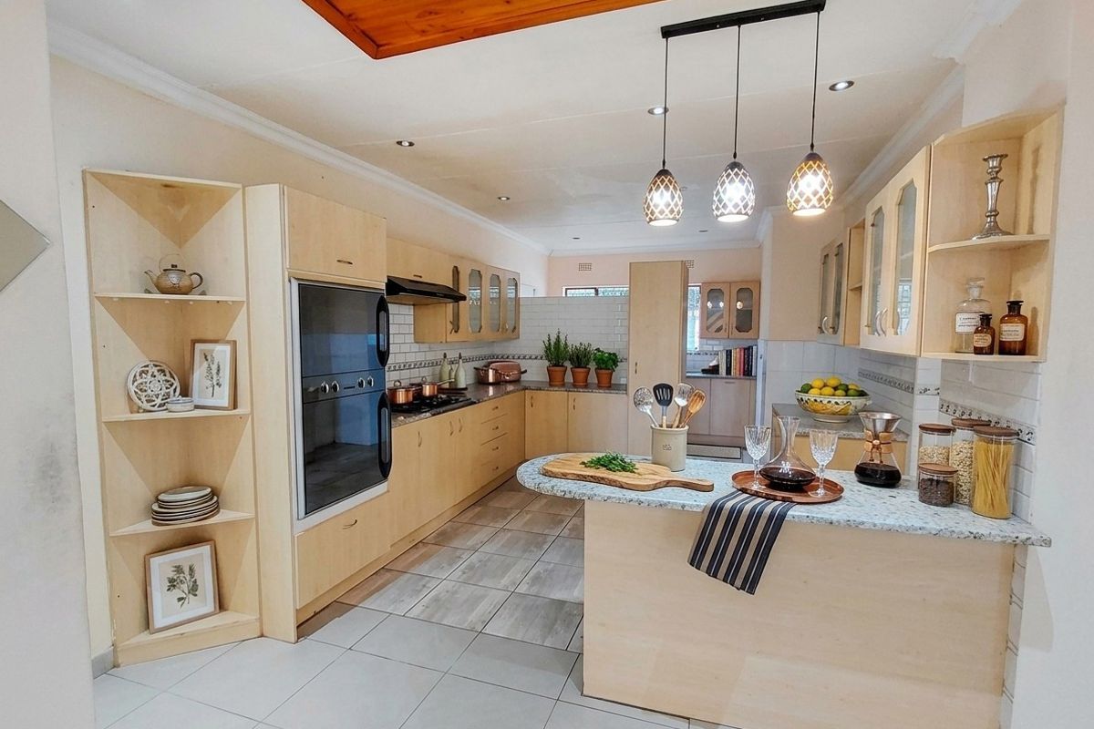 Spacious kitchen featuring light wood cabinetry, granite countertops, built-in oven, hob, extractor fan, and modern tiled flooring with ample storage and prep space.