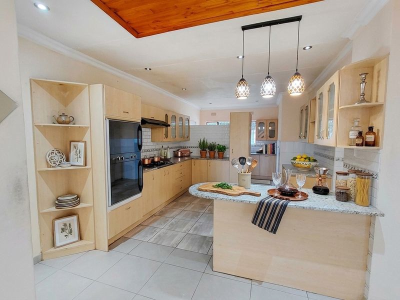 Spacious kitchen featuring light wood cabinetry, granite countertops, built-in oven, hob, extractor fan, and modern tiled flooring with ample storage and prep space.