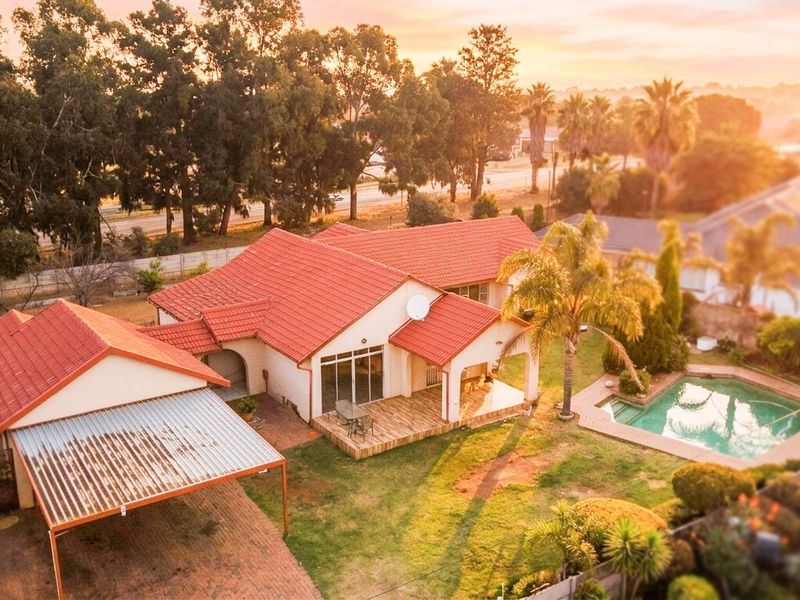 Aerial view of a residential property featuring a tiled roof house, swimming pool, covered patio, and a carport set within a landscaped garden.