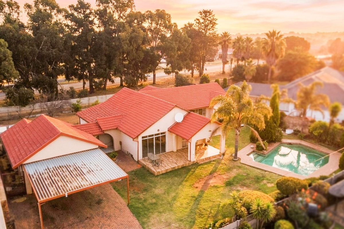 Aerial view of a residential property featuring a tiled roof house, swimming pool, covered patio, and a carport set within a landscaped garden.