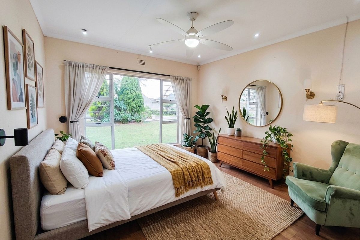 A well-maintained bedroom featuring laminate flooring, a ceiling fan, and large sliding glass doors that provide natural light and garden views.