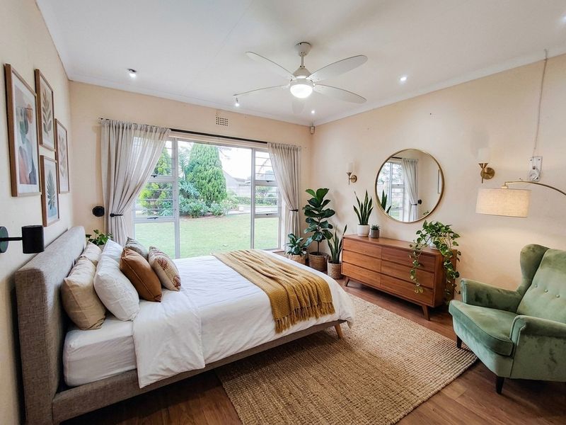A well-maintained bedroom featuring laminate flooring, a ceiling fan, and large sliding glass doors that provide natural light and garden views.