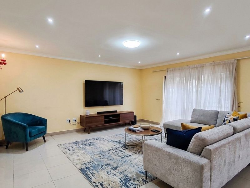 A spacious living room featuring tiled flooring, recessed downlighting, and a large sliding glass door providing natural light.