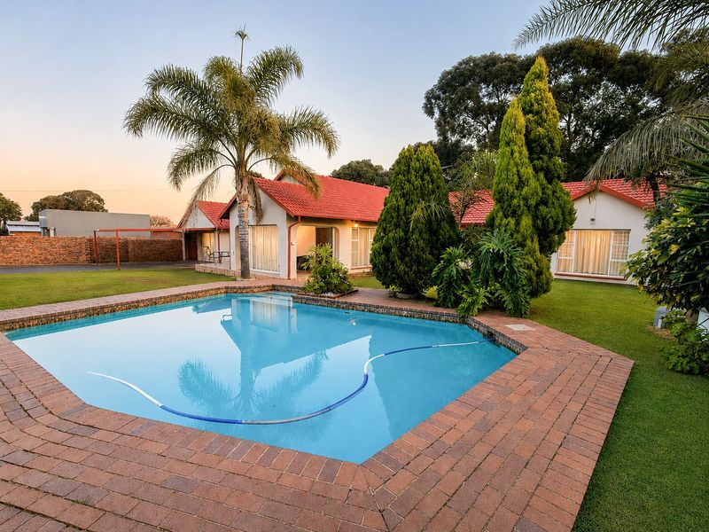 A well-maintained swimming pool area featuring brick coping, surrounded by a lush garden and the rear elevation of the house with a tiled roof.