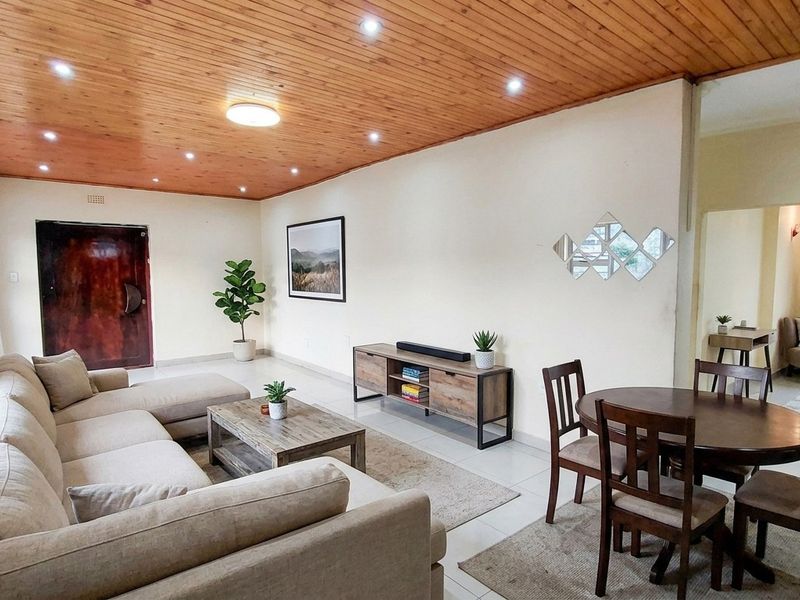 Spacious open-plan living and dining area featuring a warm timber ceiling, recessed lighting, and neutral tiled flooring throughout.