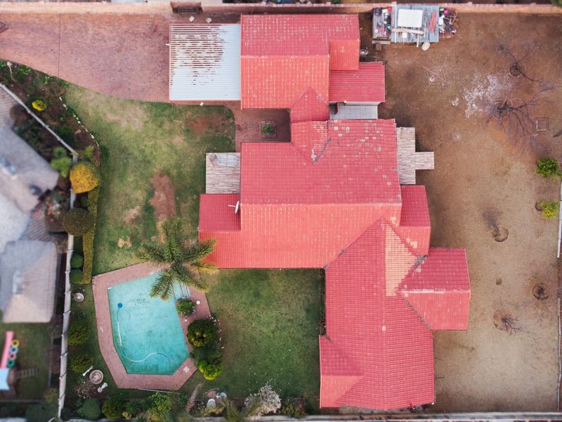 Aerial view of a residential property featuring a tiled roof, swimming pool, and surrounding garden area with paved driveway.
