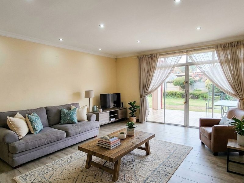 A bright and spacious living room featuring tiled flooring, recessed downlighting, and large sliding glass doors that provide direct access to the rear patio.