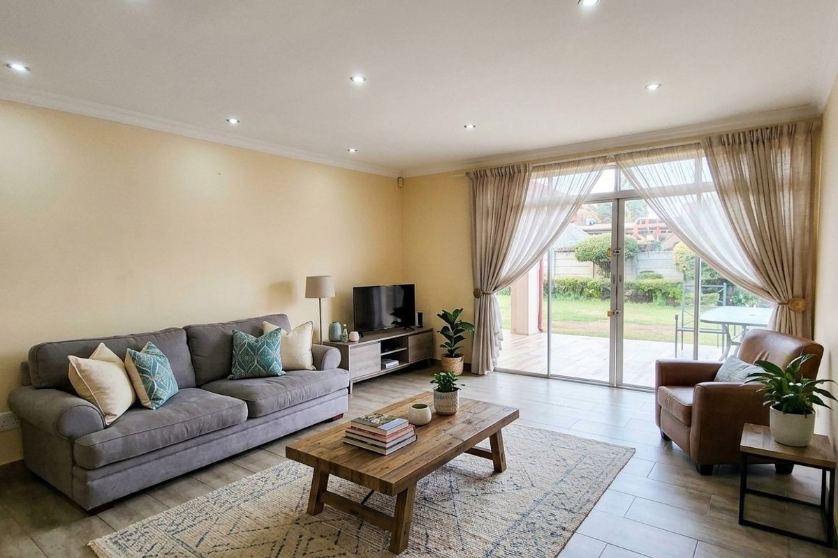 A bright and spacious living room featuring tiled flooring, recessed downlighting, and large sliding glass doors that provide direct access to the rear patio.