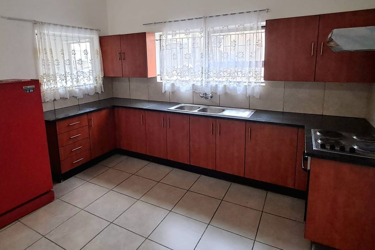 Functional kitchen featuring U-shaped cabinetry, double sink, electric hob, extractor fan, and tiled flooring with a neutral backsplash.